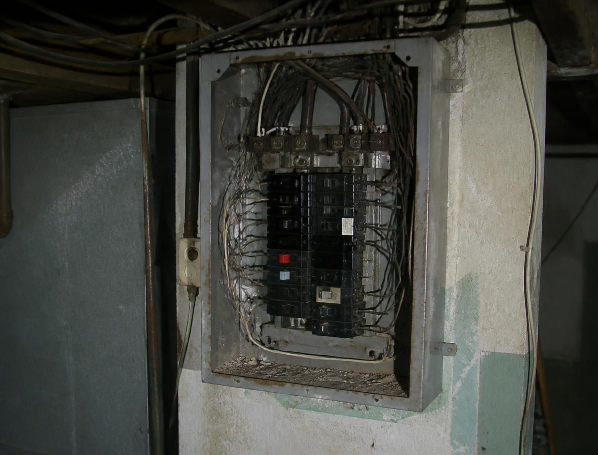 Old rusted fuse panel with tangled wiring before replacement